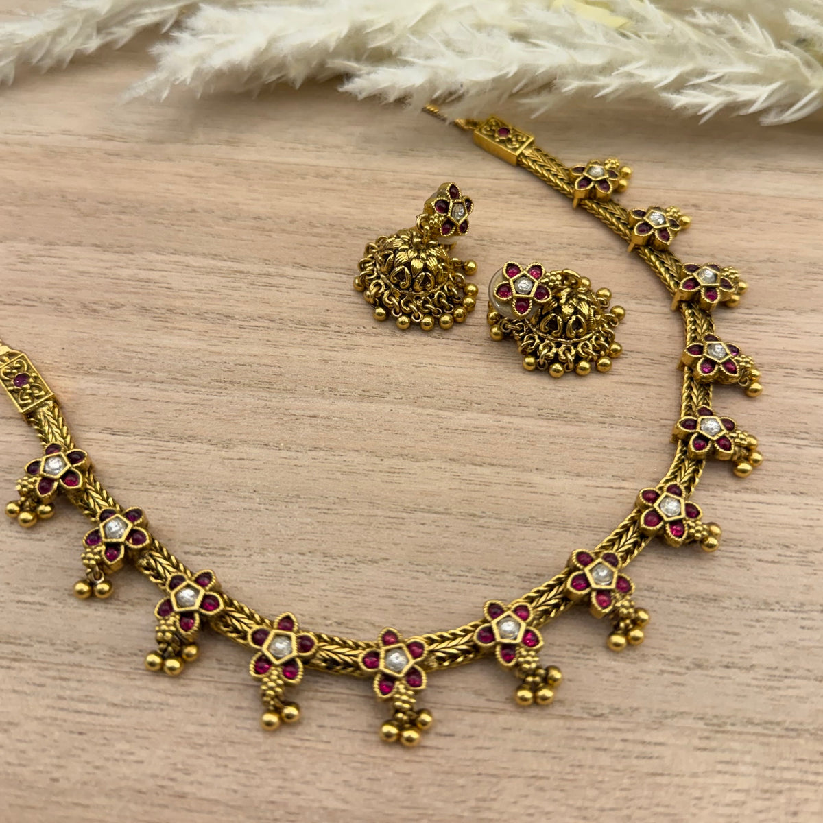 Traditional antique gold-tone South Indian necklace set featuring Kemp Ruby and white stones in a floral design, gold bead drops, and matching jhumka earrings.
